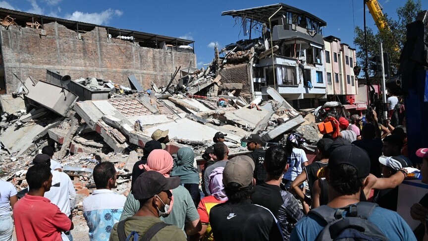 Multitud frente a un edificio urbano colapsado, con grúa, durante la cobertura de UNGRD.